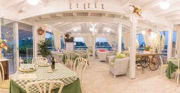 Een overdekt terras met een schouwspel van het landschap, voorzien van een geruit tafelkleed en rieten meubilair.