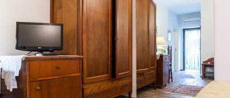 Une chambre avec une armoire en bois, un téléviseur posé sur une commode et un lit recouvert d’une couverture beige.