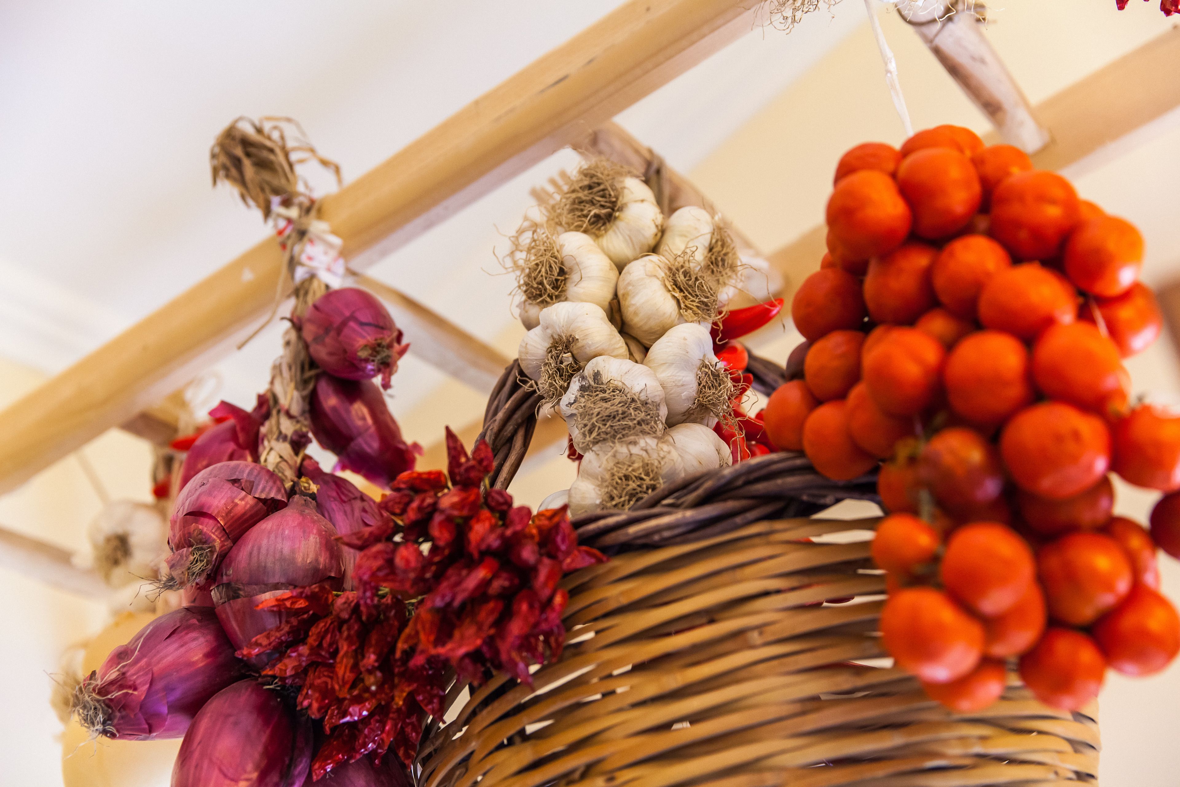 Un panier en osier contenant des têtes d’ail, des oignons rouges et des piments rouges.