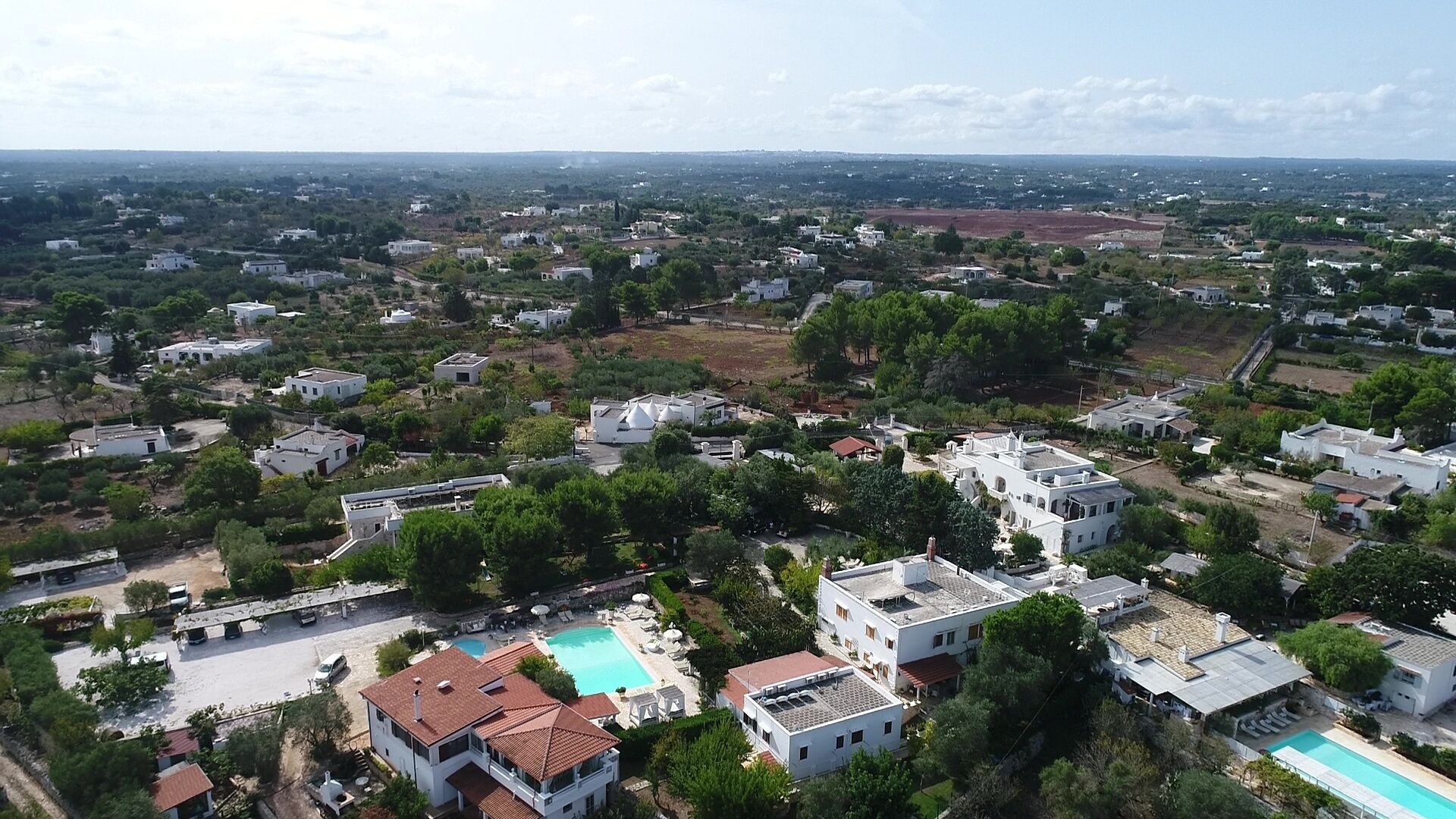 An aerial view of a residential area with multiple houses, a swimming pool, and a large open field in the background.