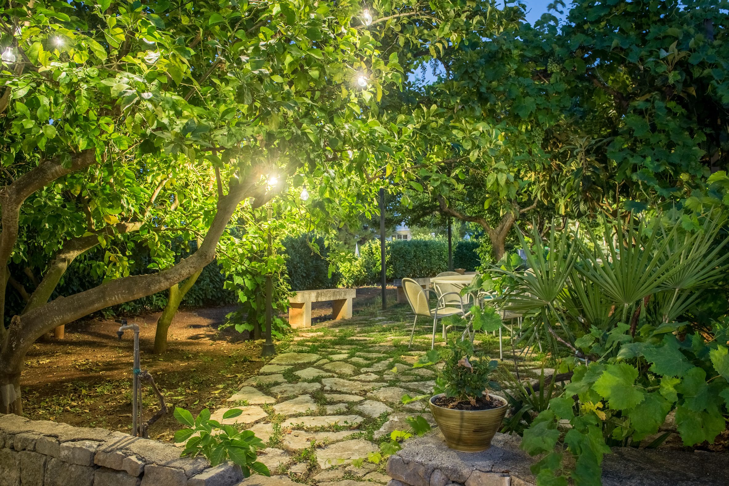 A stone-paved garden with a seating area, potted plants, and a water feature.