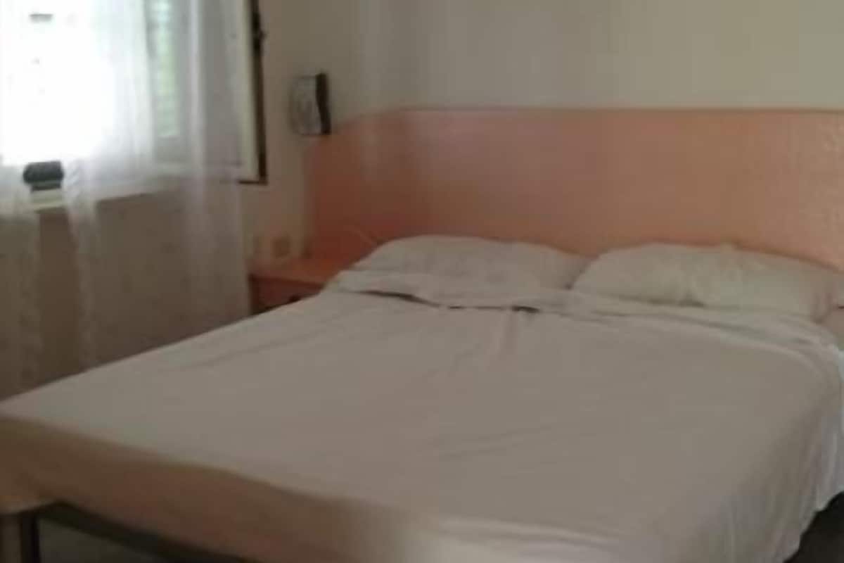 Une chambre avec un lit simple, une table de chevet et une fenêtre avec des rideaux.