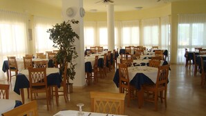 A dining area with multiple tables set for service, wooden chairs, and a large potted plant. - Villaggio Piano Grande (Vieste)