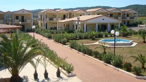 A hotel with multiple two-story buildings, a swimming pool, and a landscaped garden with palm trees. - Villaggio Piano Grande (Vieste)