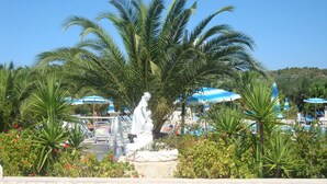 A pool area with palm trees, a statue, and umbrellas. - Villaggio Piano Grande (Vieste)