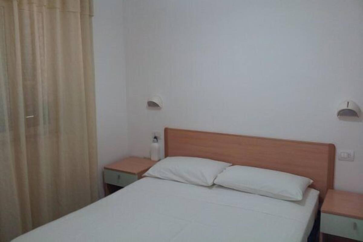 Une chambre d’hôtel simple et fonctionnelle, avec un lit simple, deux tables de chevet et un rideau.
