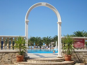 A pool area with a white archway, palm trees, and a sign with text. - Villaggio Piano Grande (Vieste)