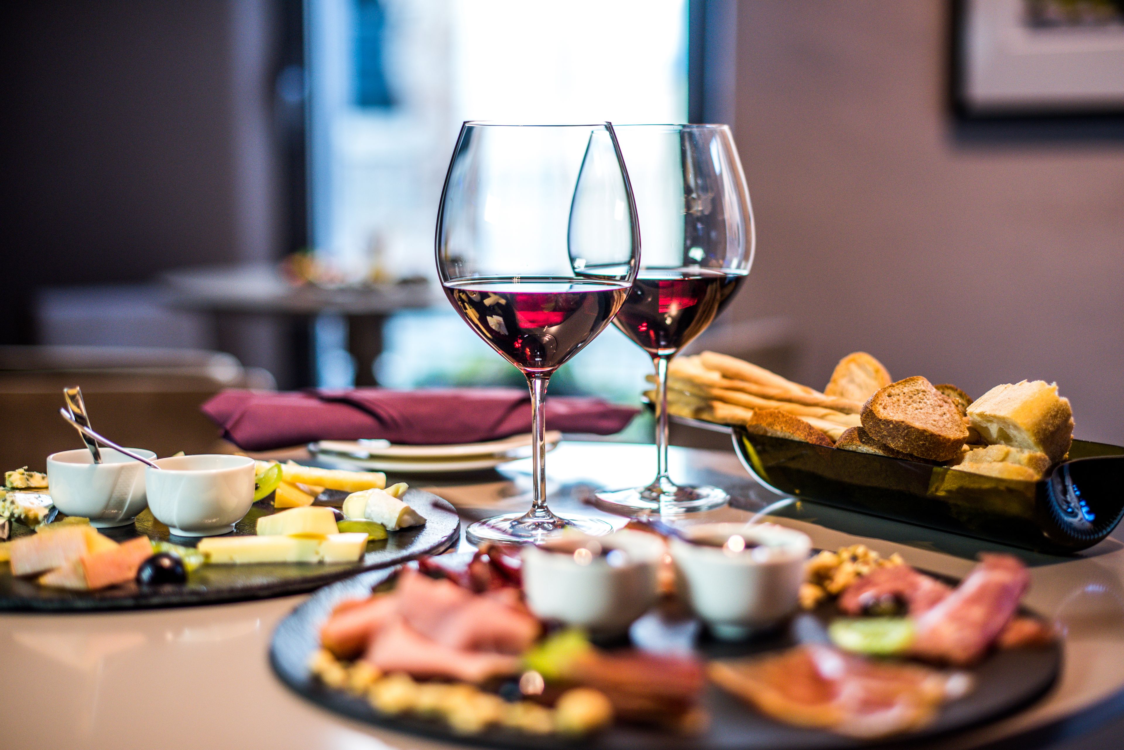 Ein Tisch mit verschiedenen Käsesorten, Wurstwaren und Brot, begleitet von zwei Gläsern Rotwein.