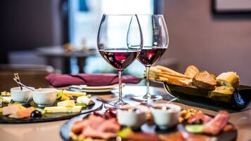 Ein Tisch mit verschiedenen Käsesorten, Wurstwaren und Brot, begleitet von zwei Gläsern Rotwein.