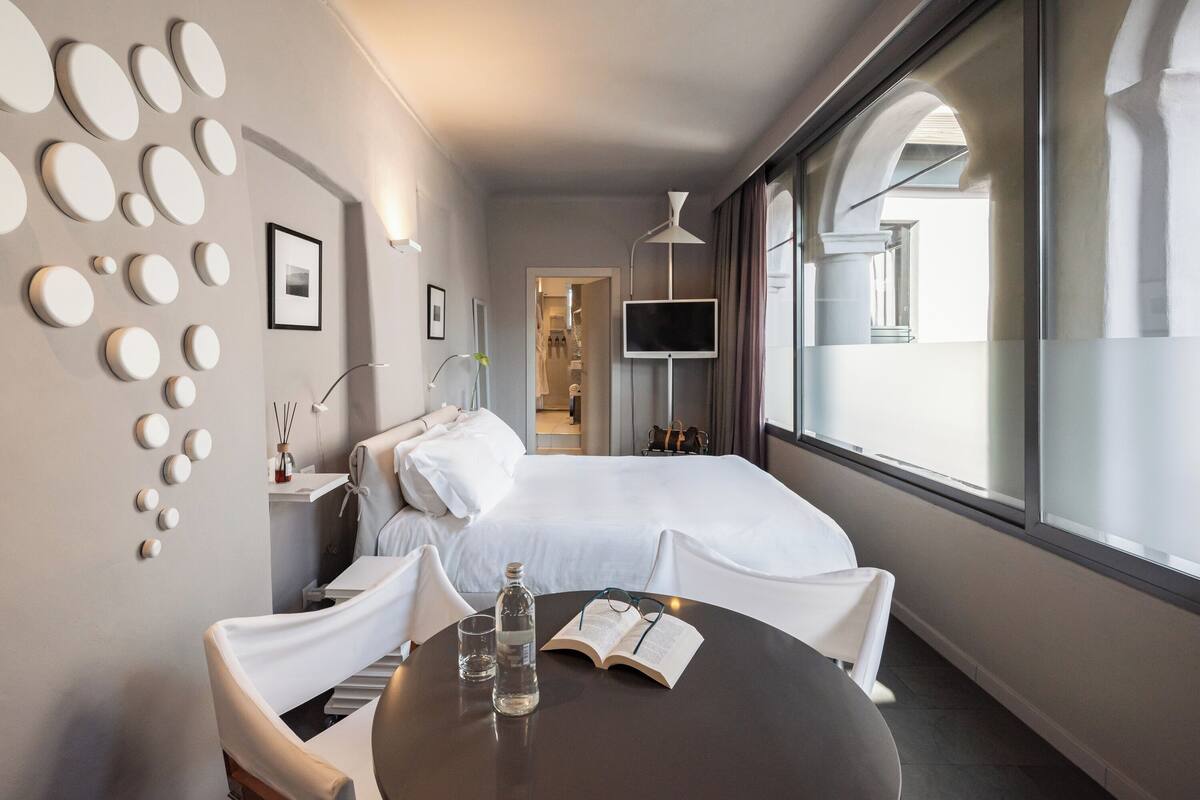 Une chambre d’hôtel avec un lit, une table de chevet avec une lampe, une télévision et une fenêtre avec des rideaux.