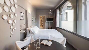 A hotel room with a bed, a bedside table with a lamp, a TV, and a window with curtains.