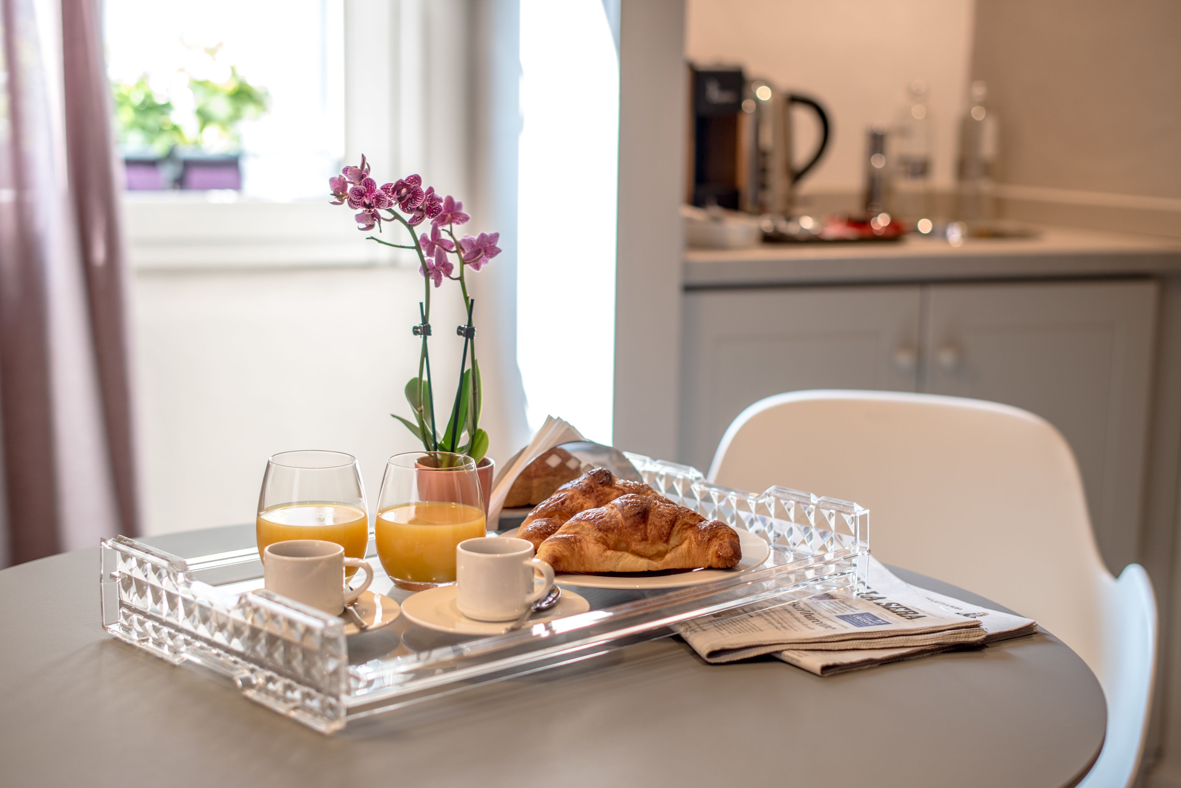 Uma bandeja de café da manhã com croissants, suco de laranja e café sobre uma mesa com um jornal.