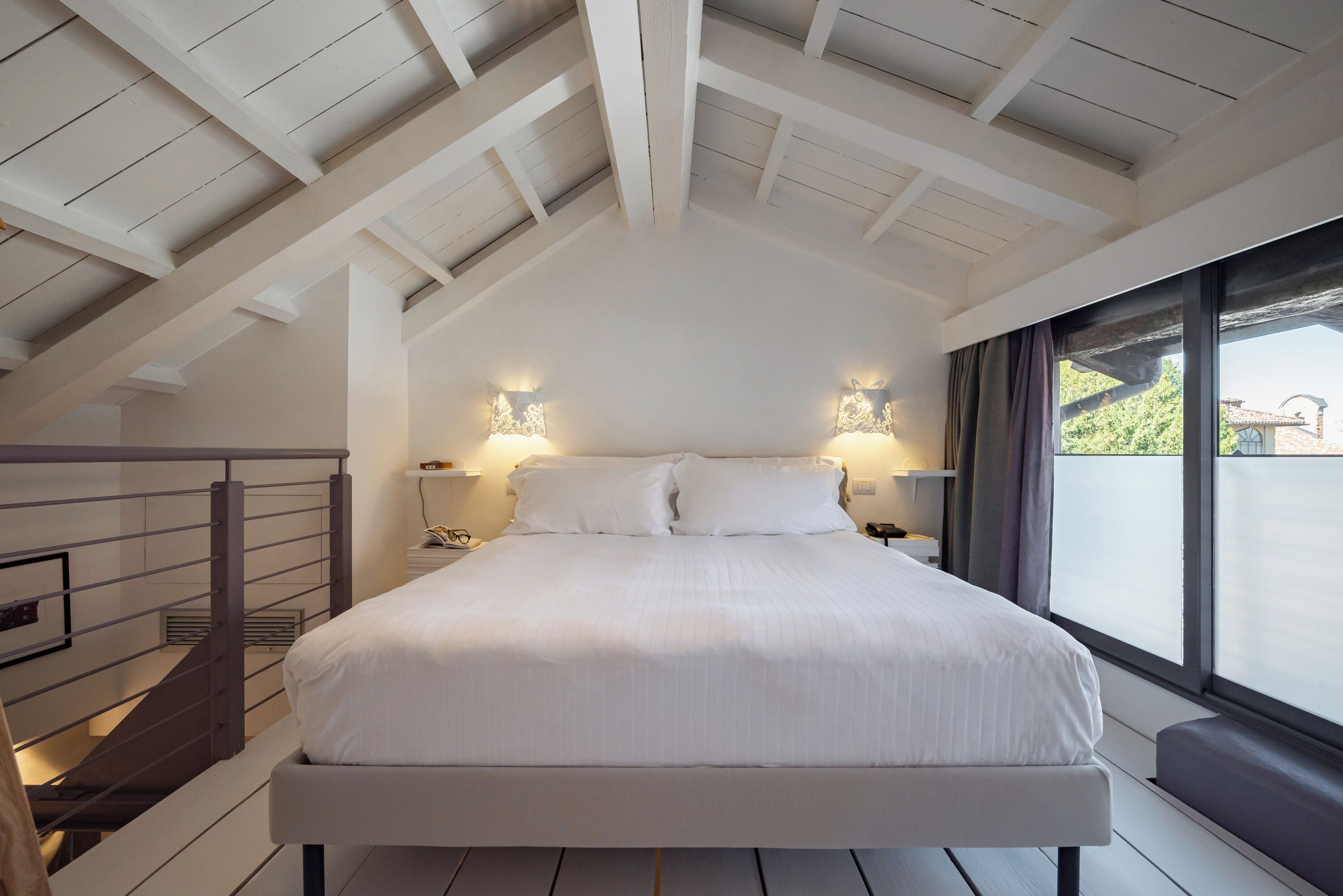 A bedroom with a large bed, wooden beams on the ceiling, and a view through a window.
