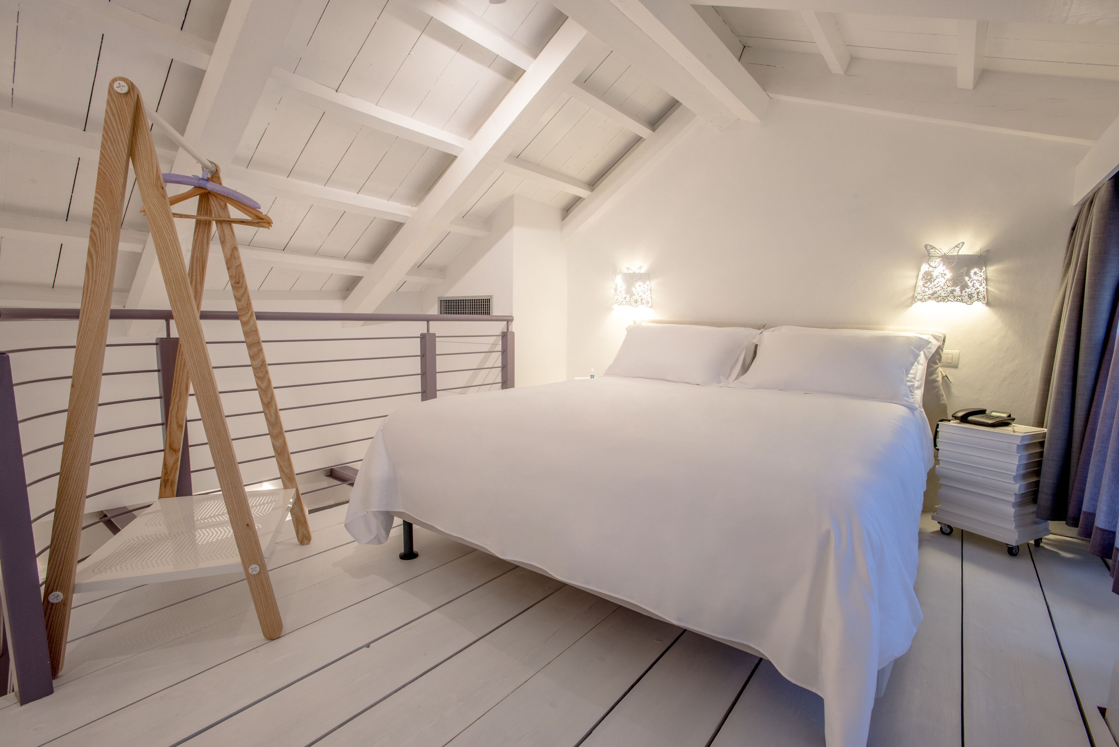 A bedroom with a wooden ladder, a bed with white bedding, and a nightstand with a lamp.