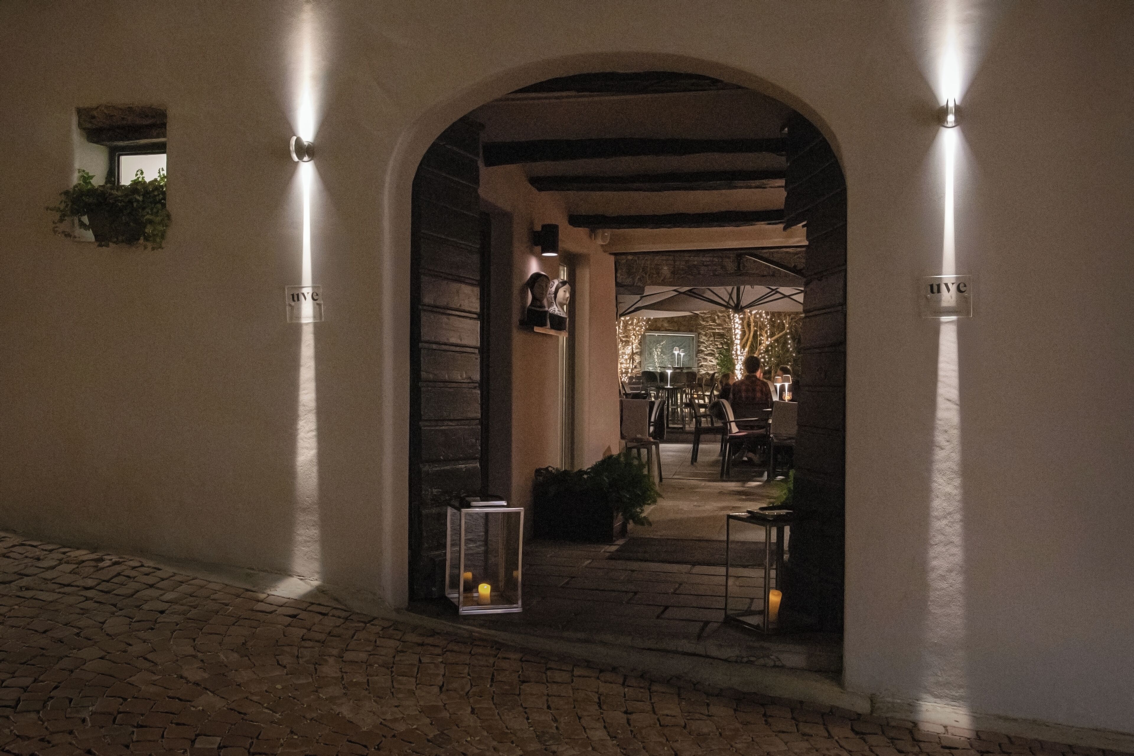 Une entrée en arc de cercle, avec un chemin pavé menant à l’intérieur, une lanterne et une enseigne portant les lettres « HVC ».