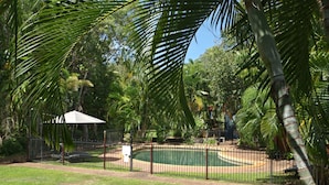 Zona de piscina cercada con palmeras y un pabellón.