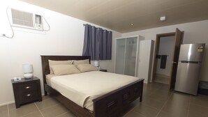 Un dormitorio con cama, mesita de noche, lámpara, aire acondicionado, armario y refrigerador.