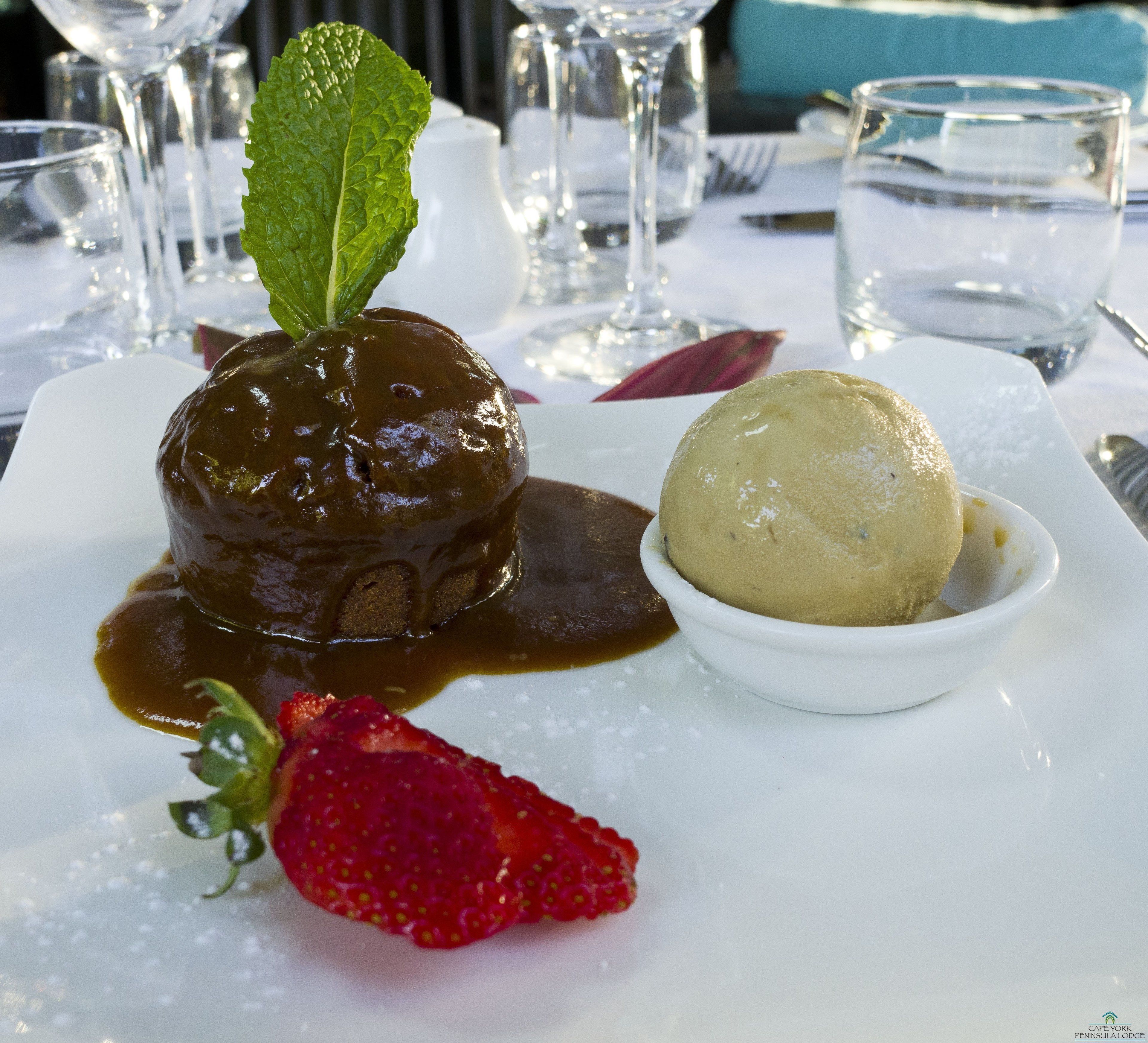 A dessert plate with a chocolate lava cake, a scoop of vanilla ice cream, and a strawberry.