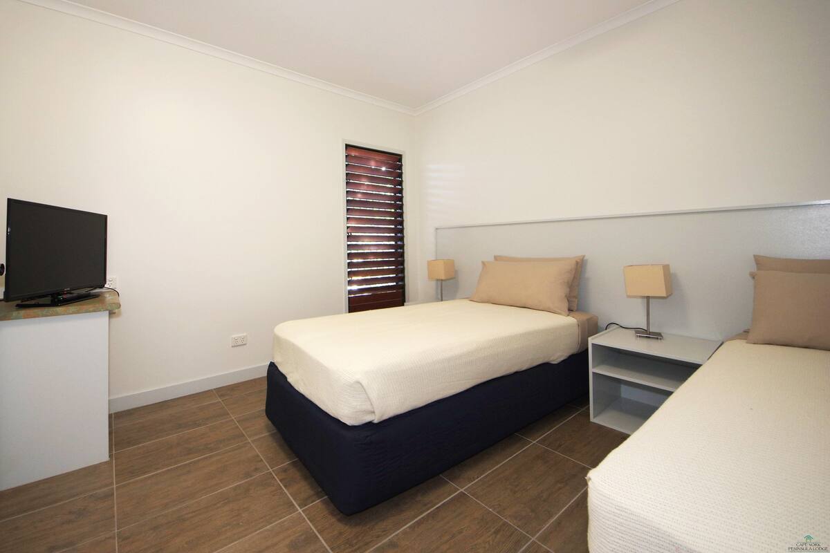 A hotel room with a bed, bedside tables, a TV, and a window with blinds.