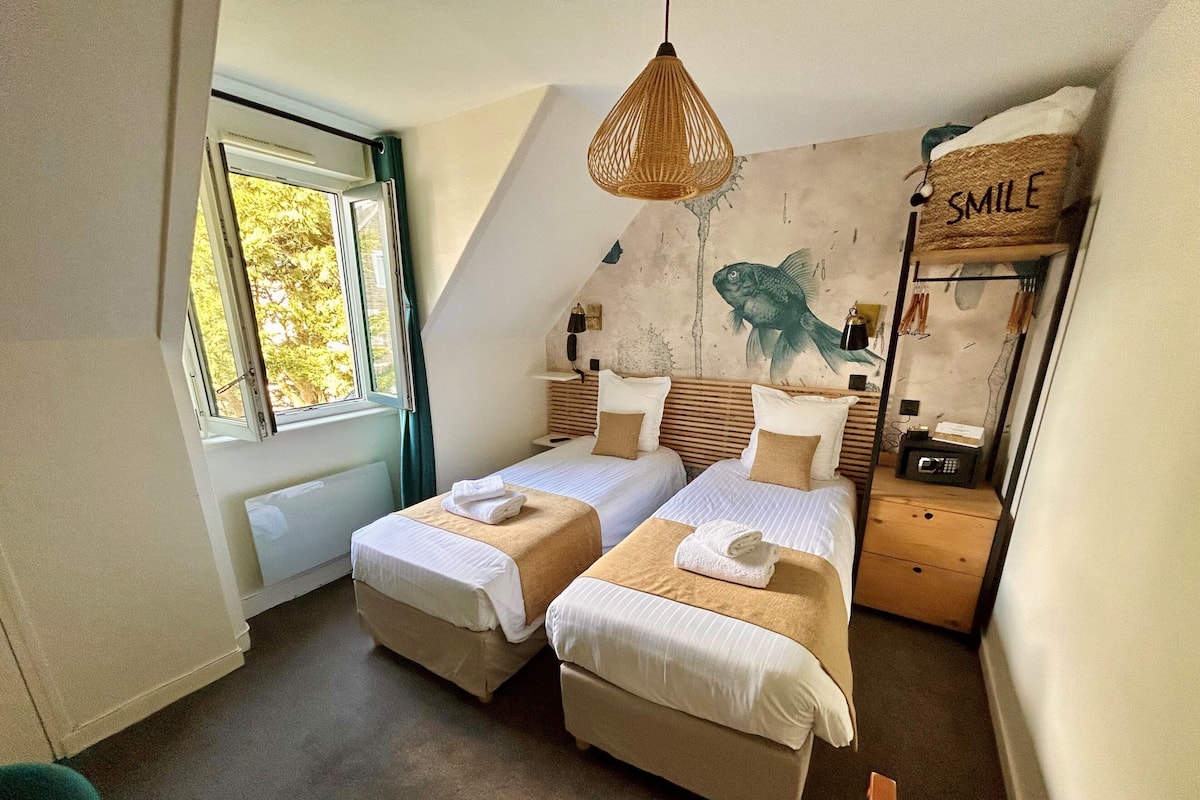 Een slaapkamer met twee bedden, een raam, een muurschildering van vissen en een bordje met de tekst 'SMILE'.