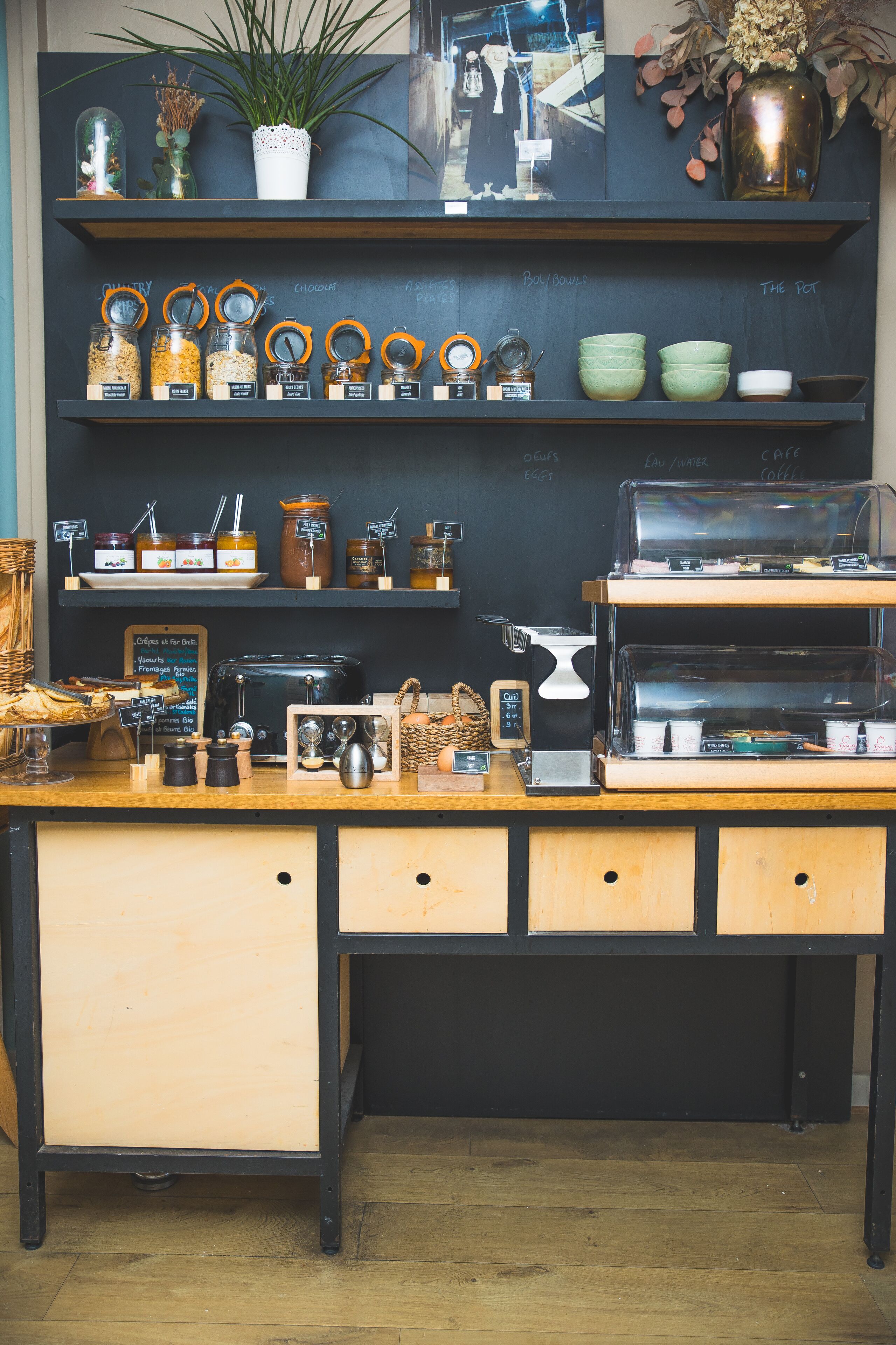 A coffee shop counter with jars of condiments, a coffee machine, and a chalkboard menu.