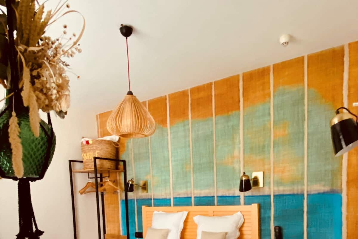 Een hotelkamer met een bed, een aan de muur bevestigd telefoon, een hanglamp en een decoratieve plant.