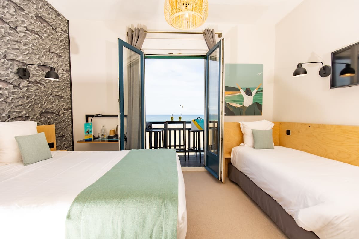 Een hotelkamer met twee bedden, een stenen muur, een balkon met uitzicht en een schilderij.