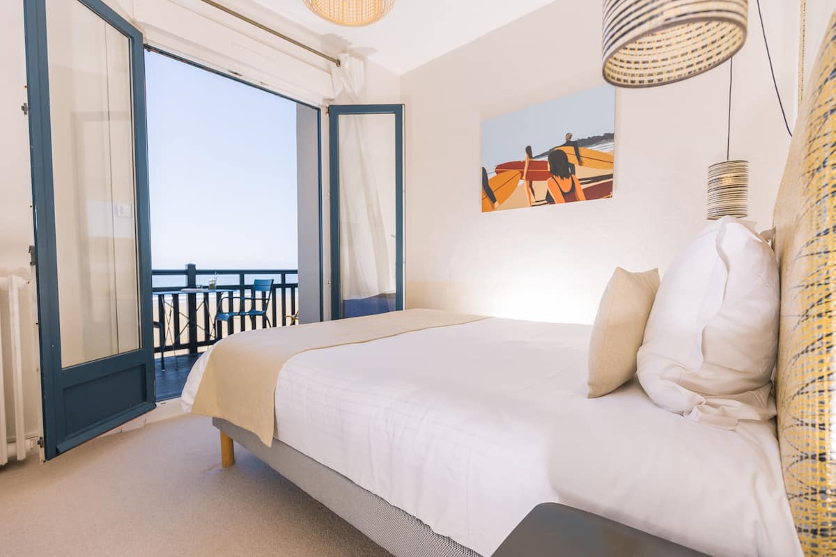 Een slaapkamer met een groot bed, uitzicht op een balkon en een schilderij aan de muur.