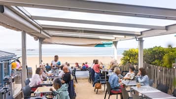 An outdoor café with tables and chairs, overlooking a beach.