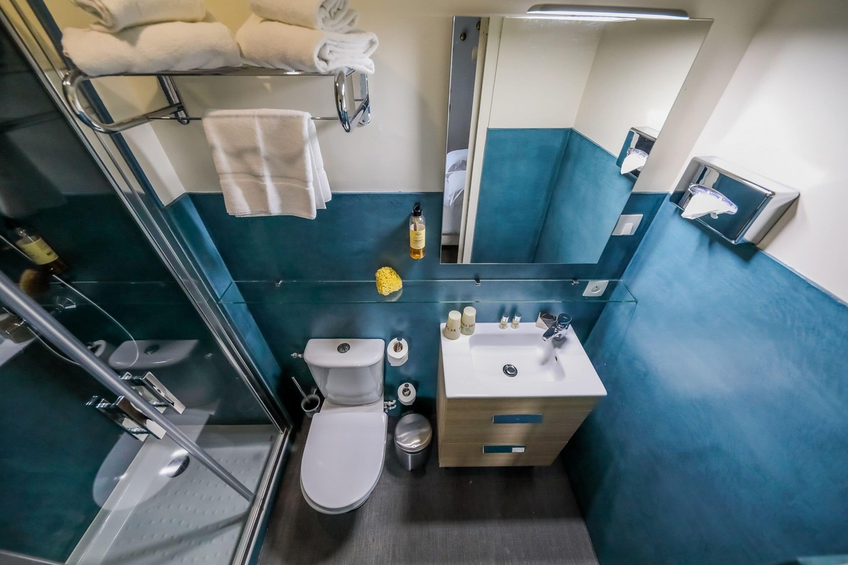 Un baño pequeño con cabina de ducha de vidrio, inodoro blanco, lavabo con espejo y toallero con toallas dobladas.