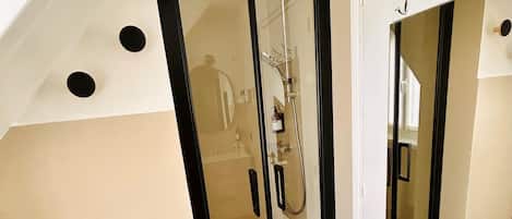 A modern bathroom with a glass shower enclosure, a white vanity, and a mirror with hooks.