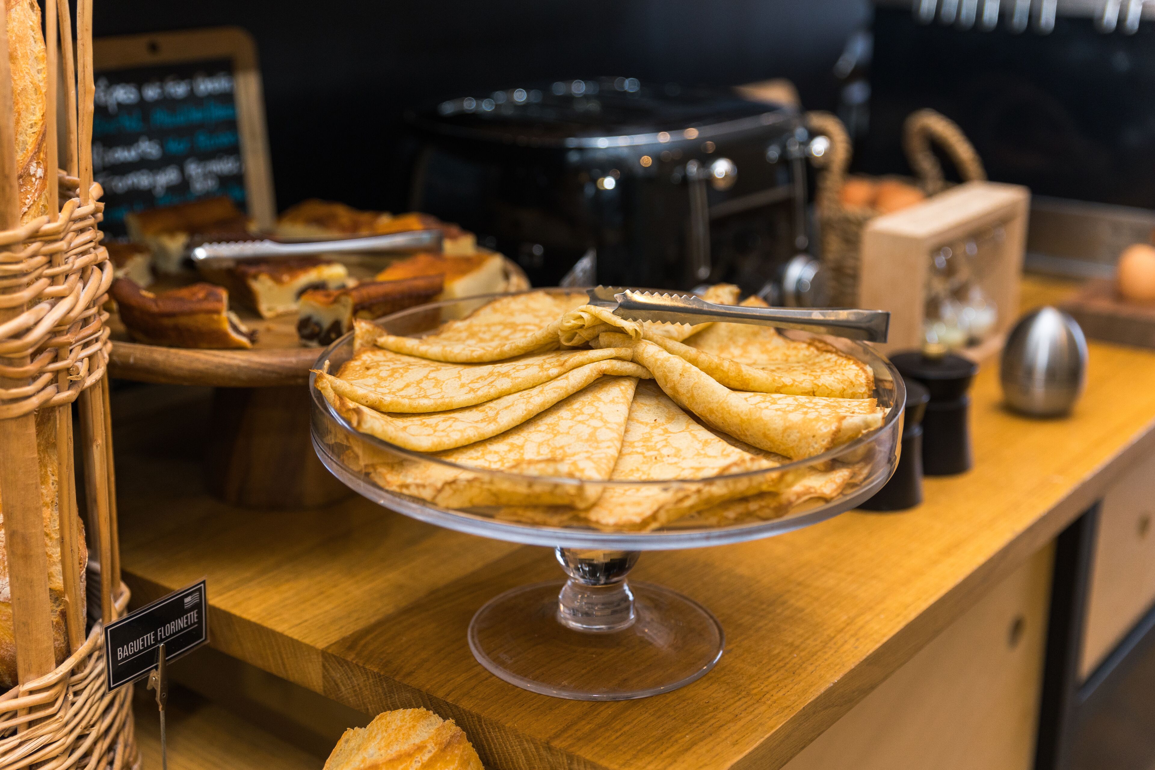 Una vitrina de panadería exhibe crepes, un letrero que dice 'Baguette Florentine' y diversas herramientas e ingredientes de repostería al fondo.