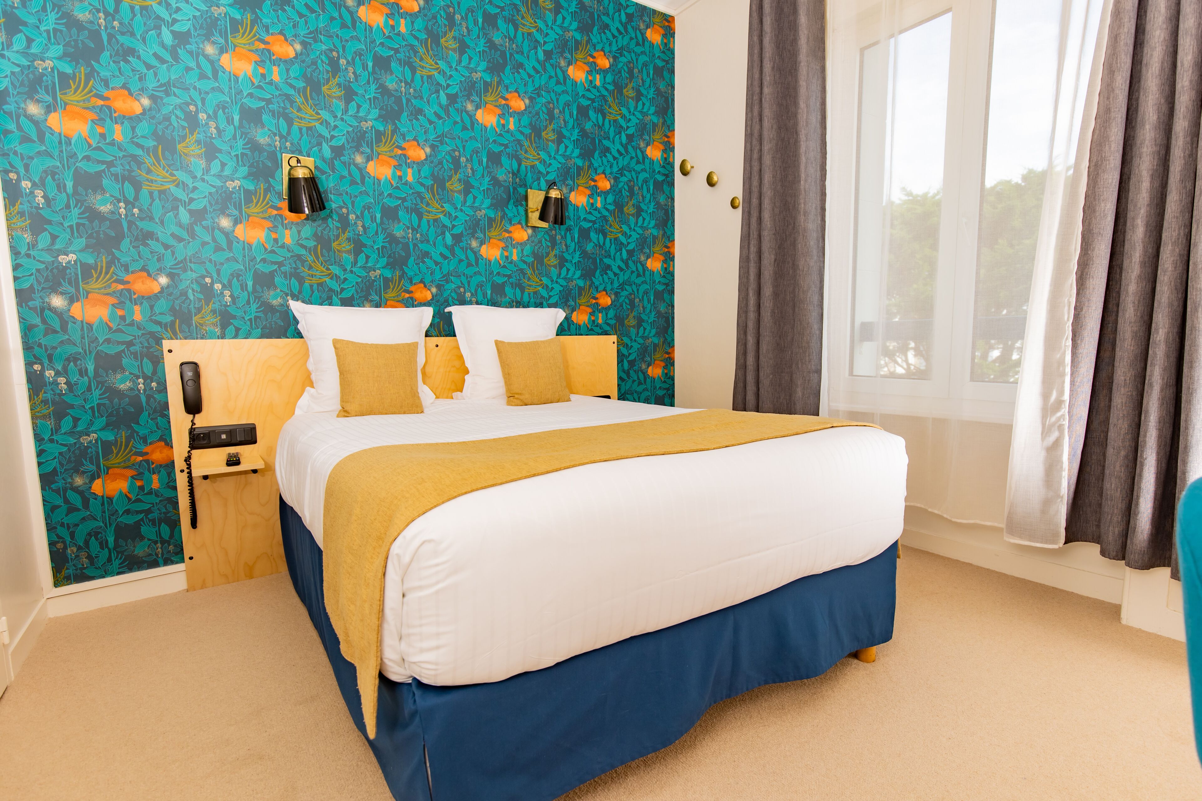 A hotel room with a bed, a nightstand, a telephone, and a window with curtains.
