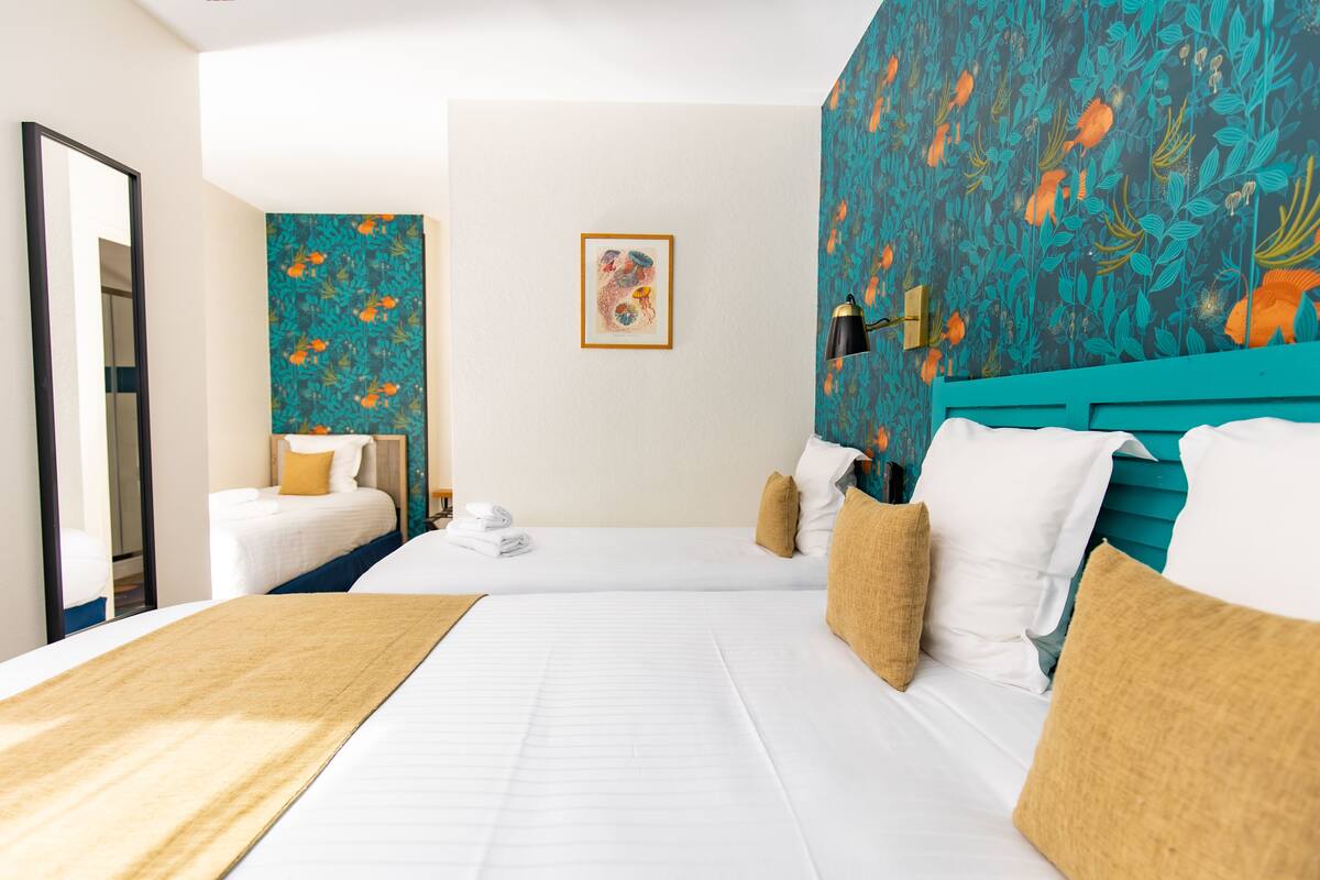 Een hotelkamer met twee bedden, een grote spiegel, een muur met een vispatroon en een ingelijst schilderij.