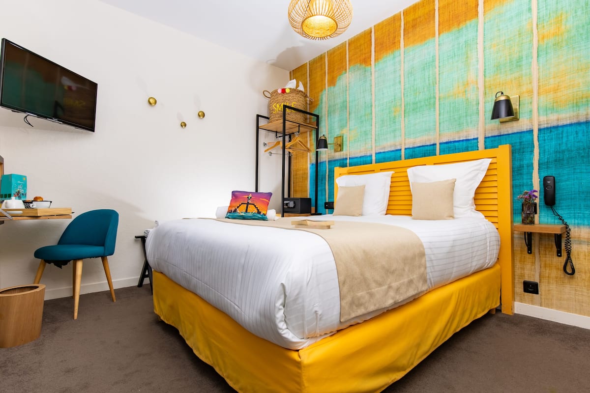 Een hotelkamer met een bed, een bureau, een stoel, een televisie en een kleurrijke wand.