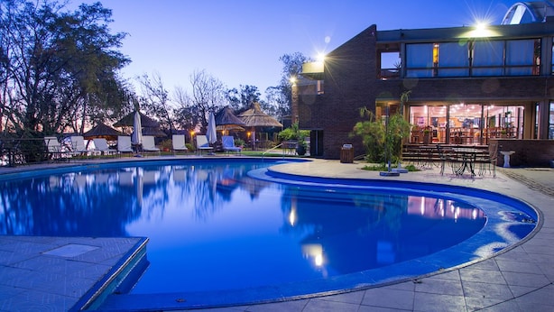 A swimming pool with lounge chairs and umbrellas, a restaurant with outdoor seating, and a building with large windows.