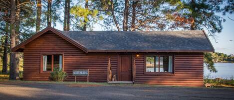 A log cabin with a sloped roof, a front door, and a window.