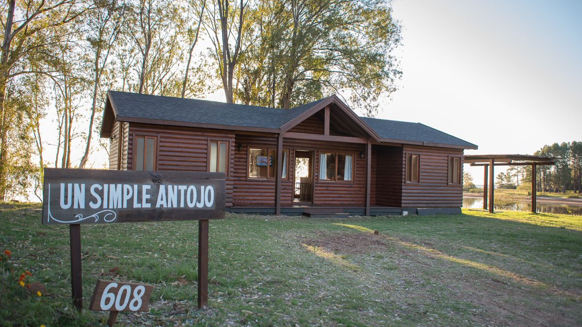 A log cabin with a sign reading "UN SIMPLE ANTOJO 608" in front.