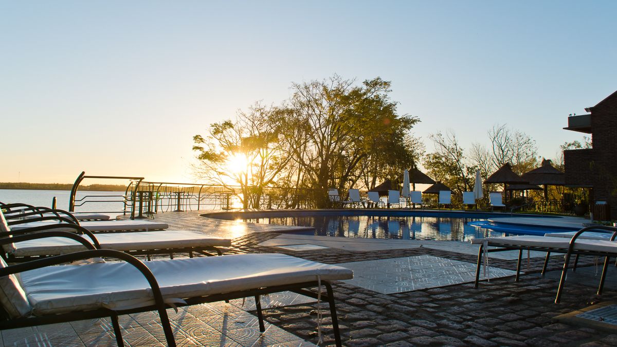 A poolside area with lounge chairs and umbrellas, a clear sky, and a sunset.