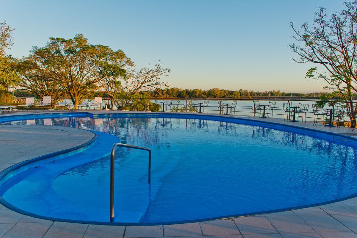 Una piscina de borde curvo, rodeada por una barandilla metálica y árboles.