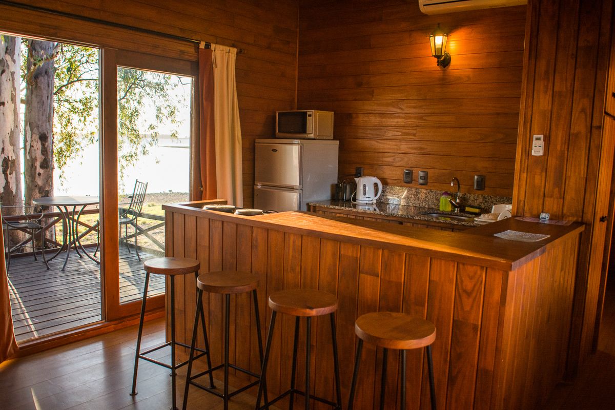 Ein Holzinterieur mit Barbereich, Hockern, einem Kühlschrank, einer Mikrowelle, einem Wasserkocher und Blick ins Freie.