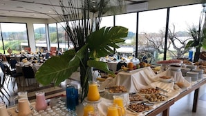 A buffet setup with various food items and beverages, surrounded by large windows offering a scenic view.