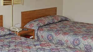A neatly made bed with a floral comforter, a bedside table with a lamp, and a framed picture on the wall. - Iron Horse Inn (Whitewood)