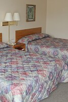 Una cama bien hecha con una colcha estampada, una mesita de noche con una lámpara y un cuadro en la pared.