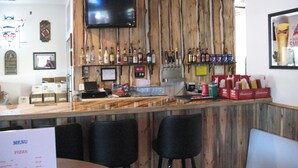 A bar area with a wooden wall, a flat-screen TV, and various bottles. There are chairs and a menu visible. - Iron Horse Inn (Whitewood)