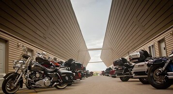 Filas de motocicletas estacionadas en un área techada de diseño simétrico, bajo un cielo despejado.