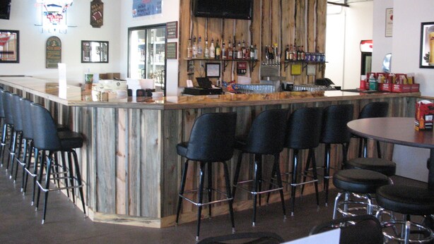 A bar area with a wooden bar counter, multiple bar stools, and a television mounted on the wall. - Iron Horse Inn (Whitewood)