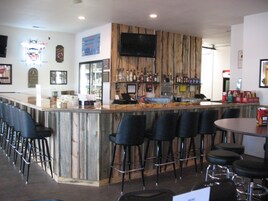 Una zona de bar con mostrador de madera, varios taburetes y un televisor montado en la pared.