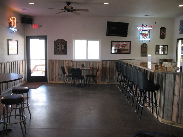 A bar area with wooden paneling, a dartboard, and a neon sign.