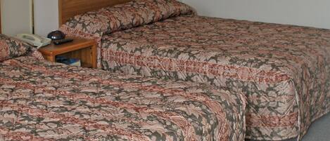 A double bed with floral bedding, a bedside table with a lamp, and a wall-mounted telephone.